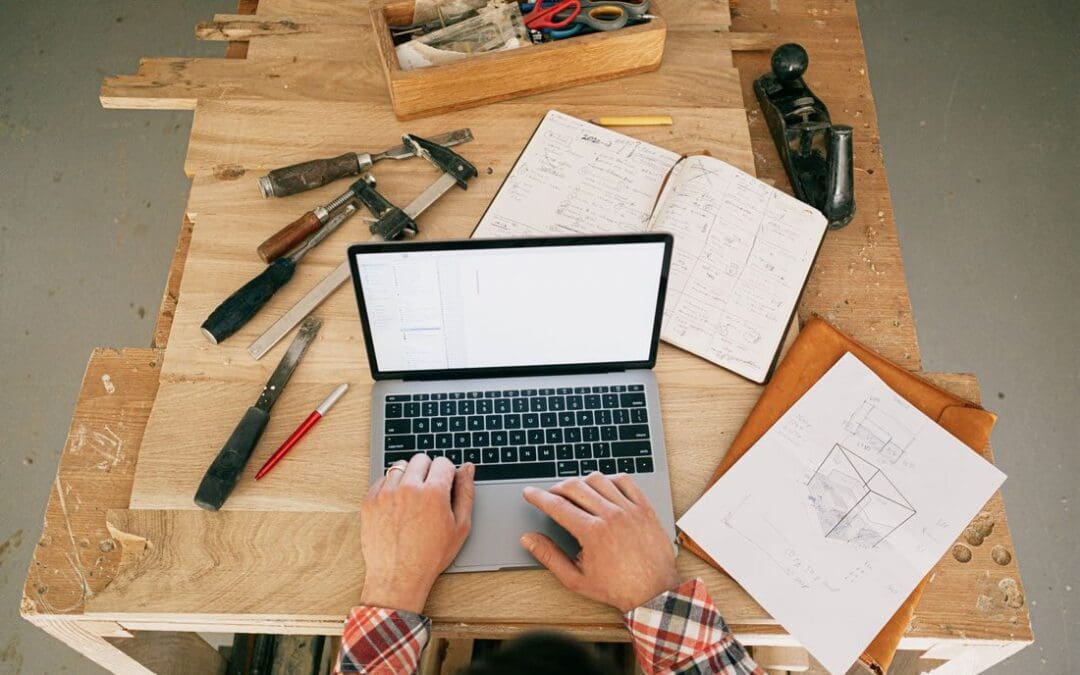 Laptop on desk surrounding by chaotic drawings and mockups of construction measurements looking at drywall efficiency