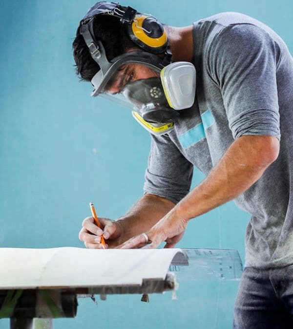 Construction worker wearing a protective mask as he measures up building material for construction compliance and safety